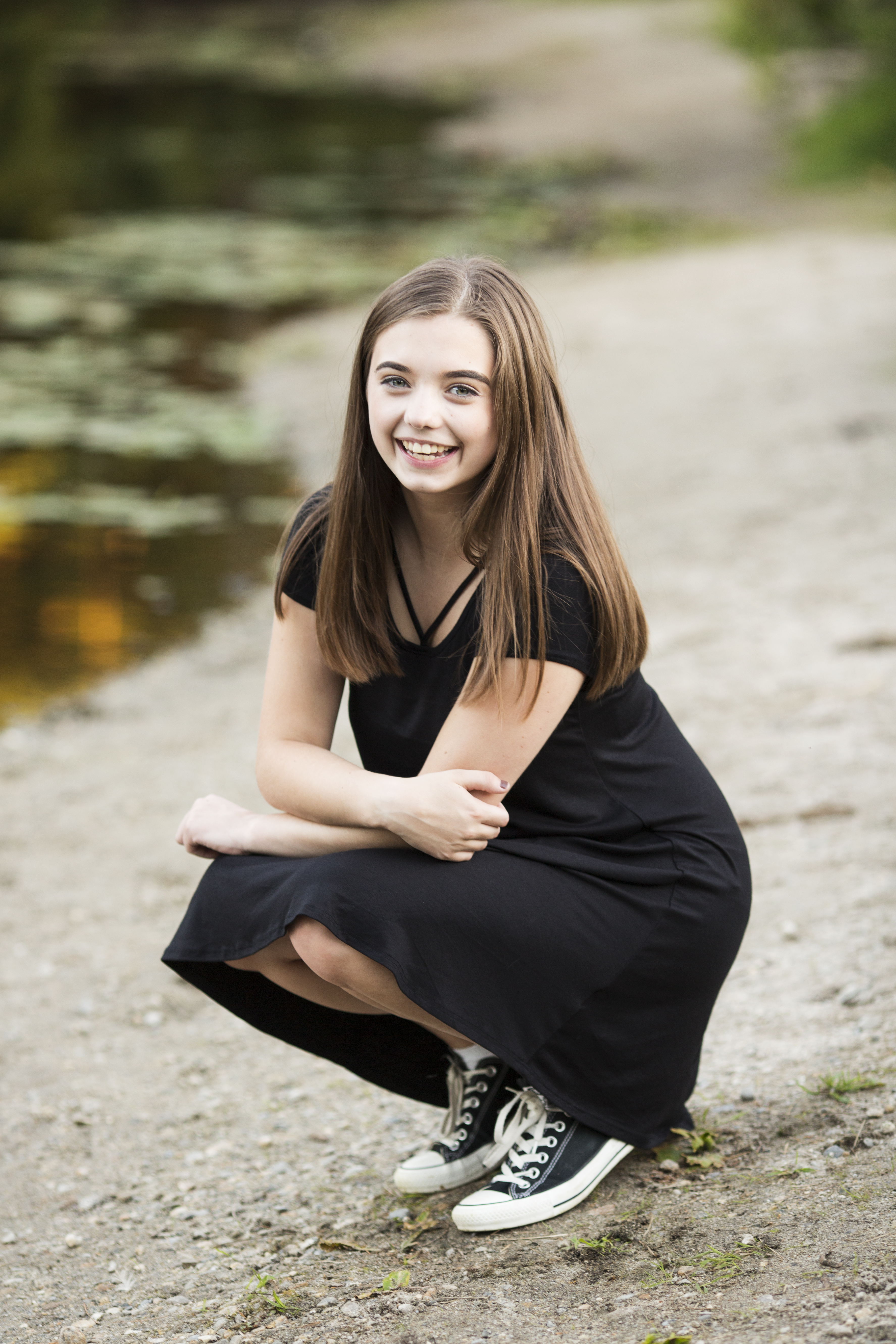 girl in black dress smiling senior portrait lakeside beach