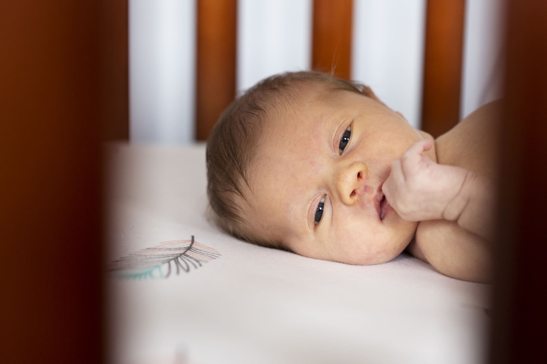 baby girl lying awake in her crib nursery feather sheets