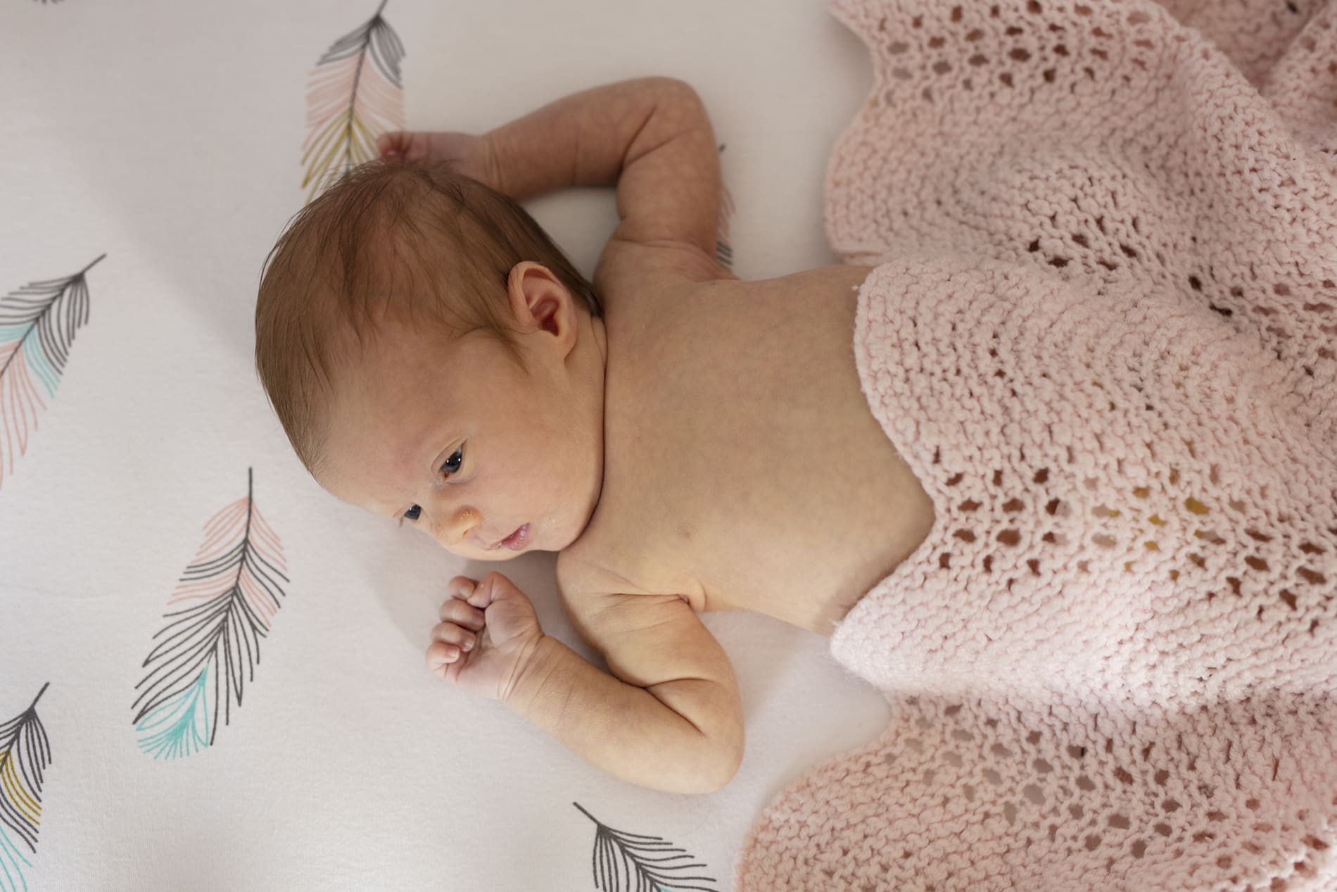 newborn baby girl lying down nursery crib awake pink afghan crochet heirloom blanket