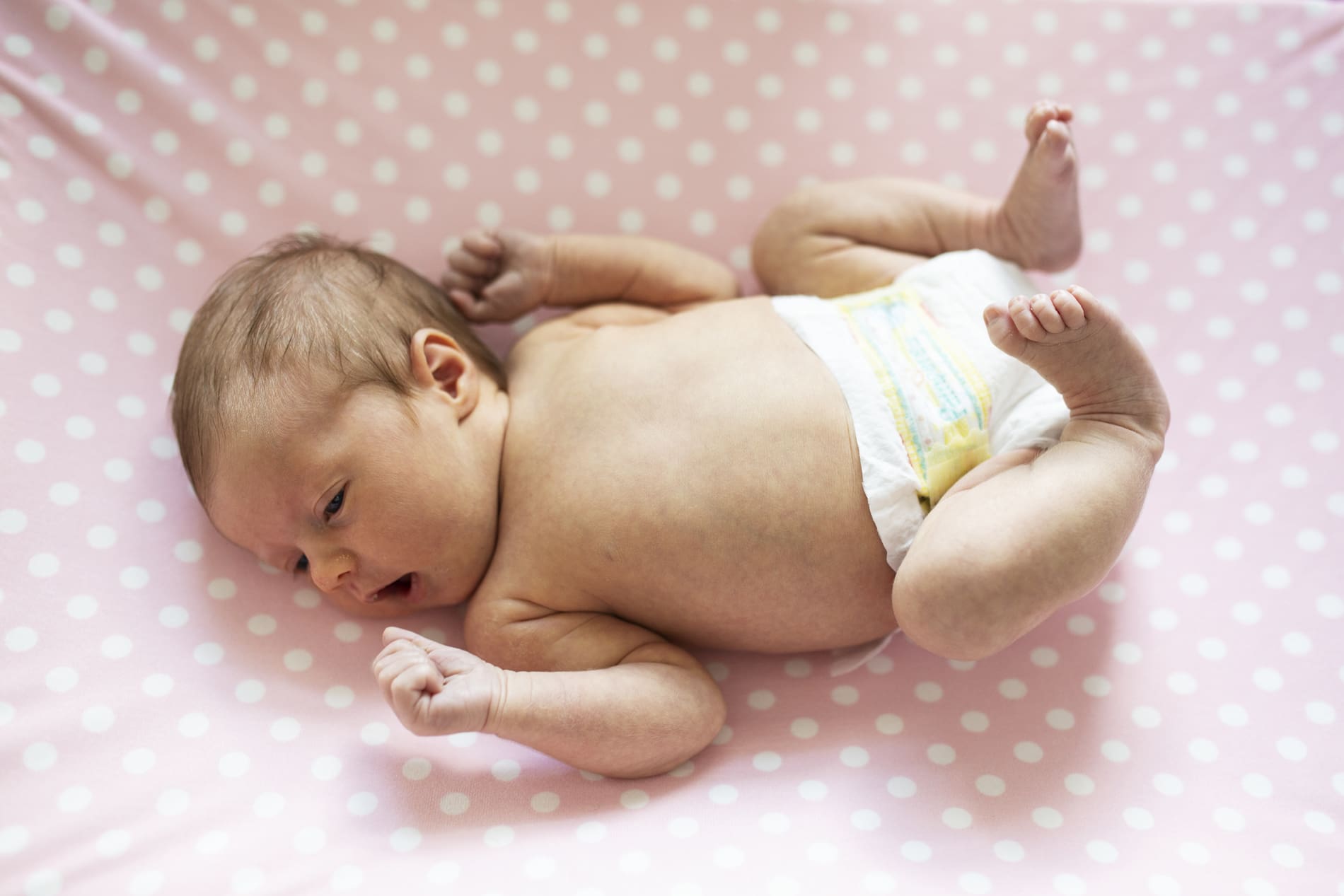 newborn baby girl lying on changing table wearing diaper pink polka dots