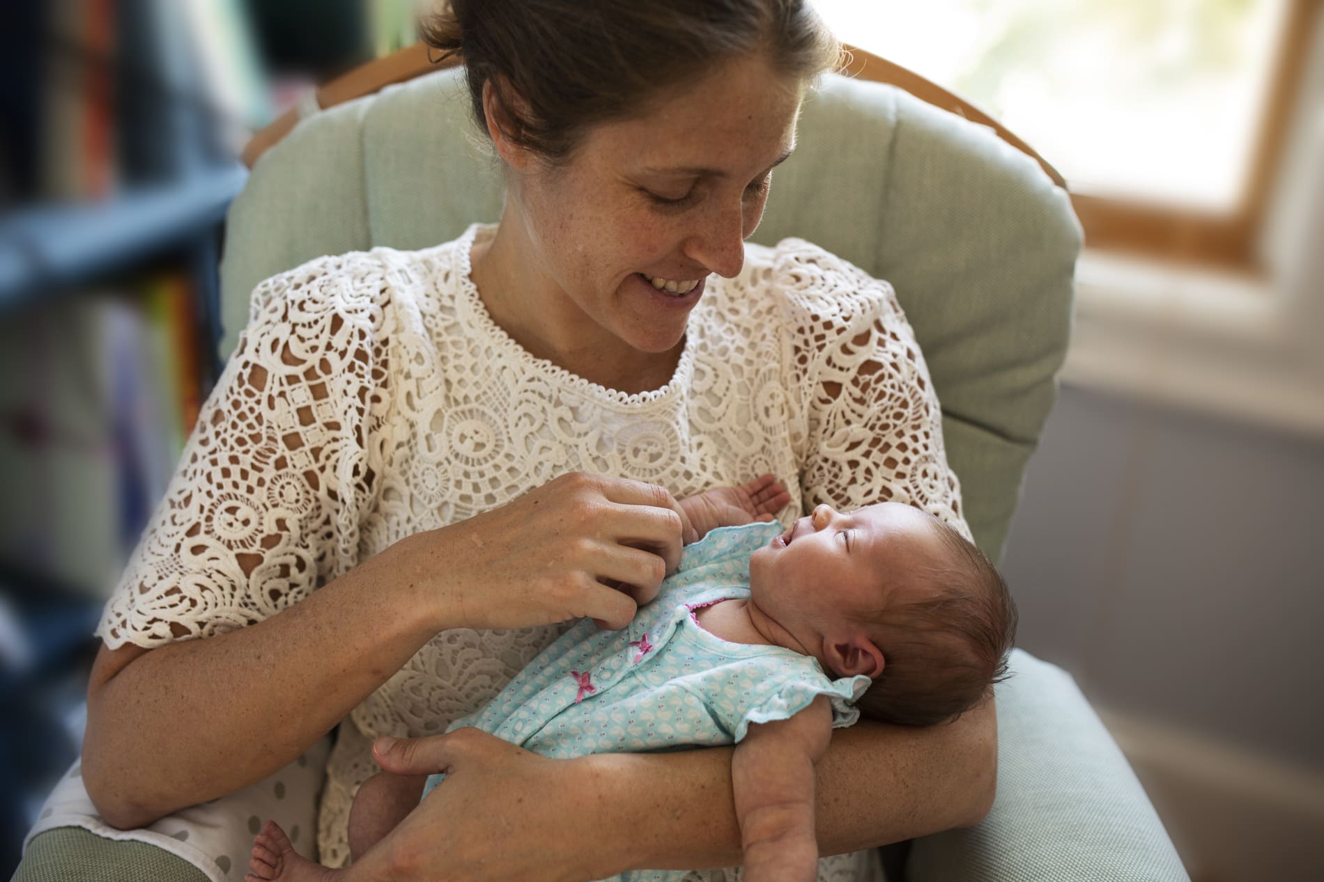 mom holding newborn baby girl nursery rocking chair smiling