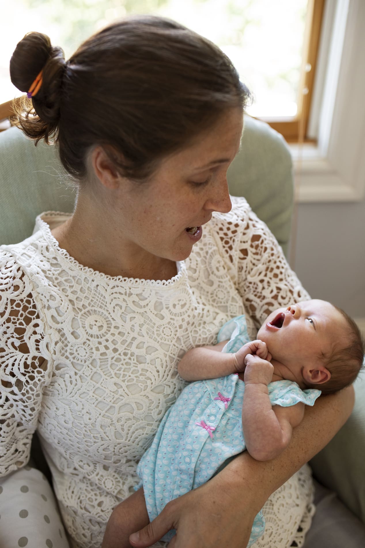 newborn baby girl yawning while holding mom arms