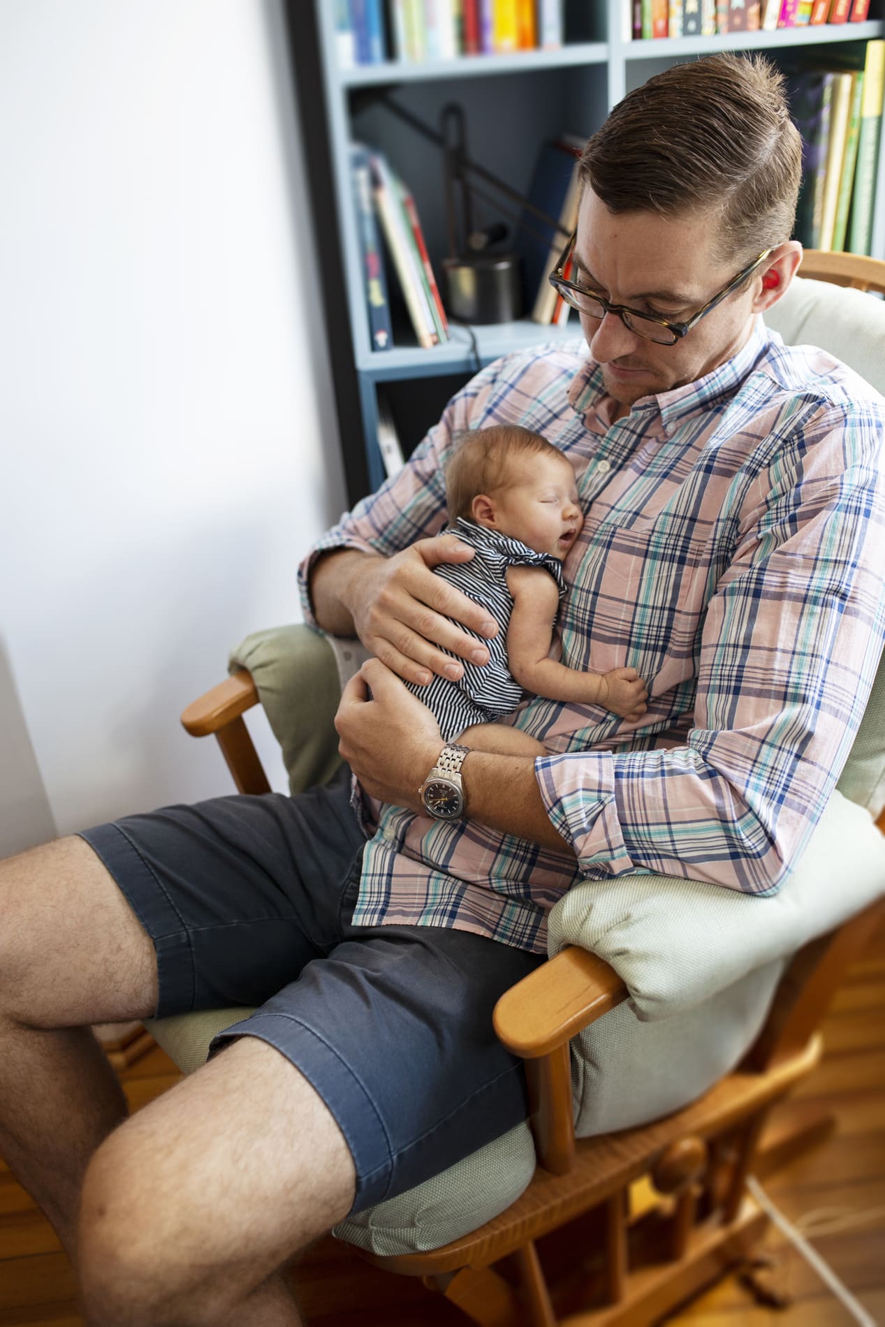 dad holding newborn baby girl on chest in nursery rocking chair
