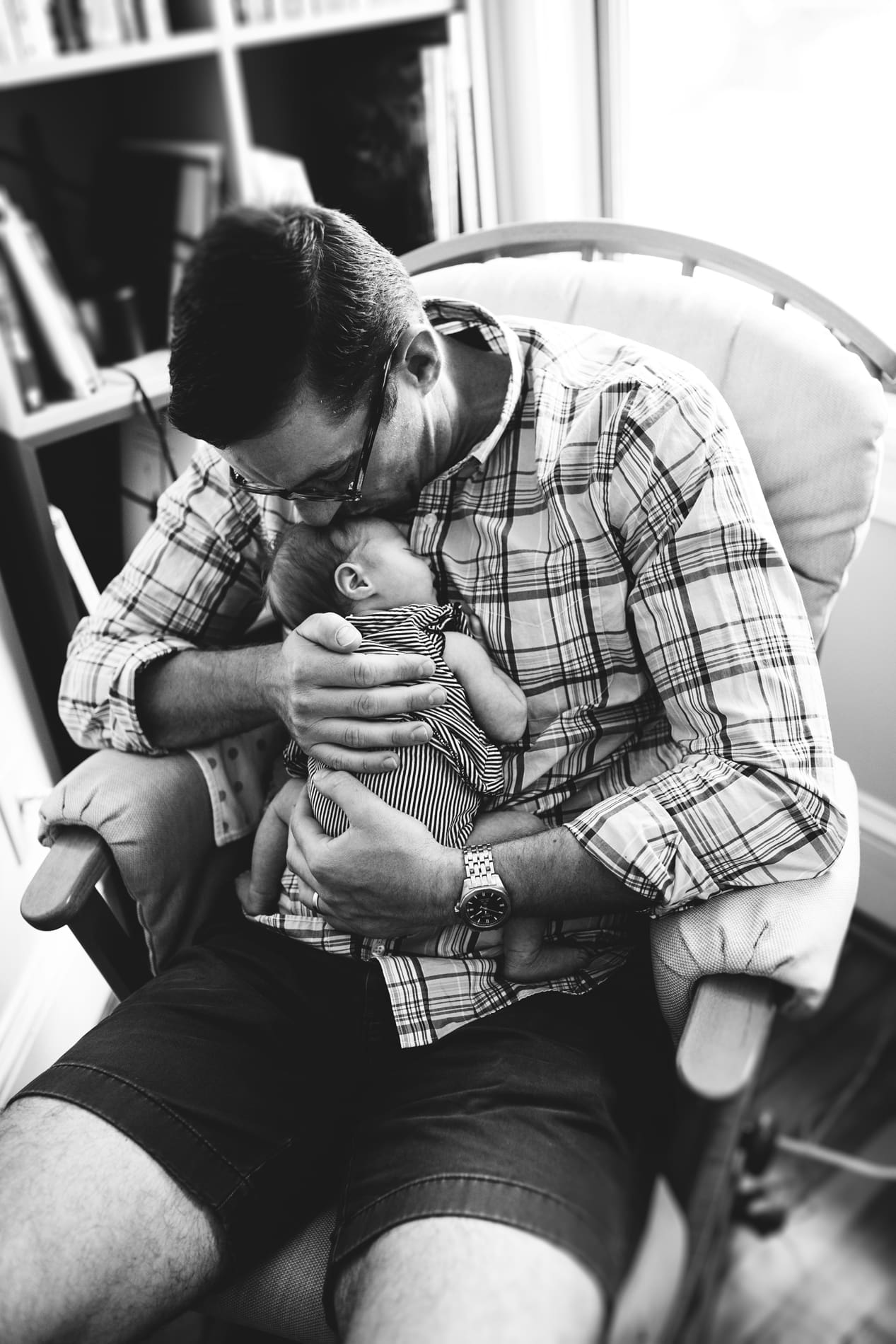 black white photo dad kisses newborn baby girl sleeping nursery rocking chair