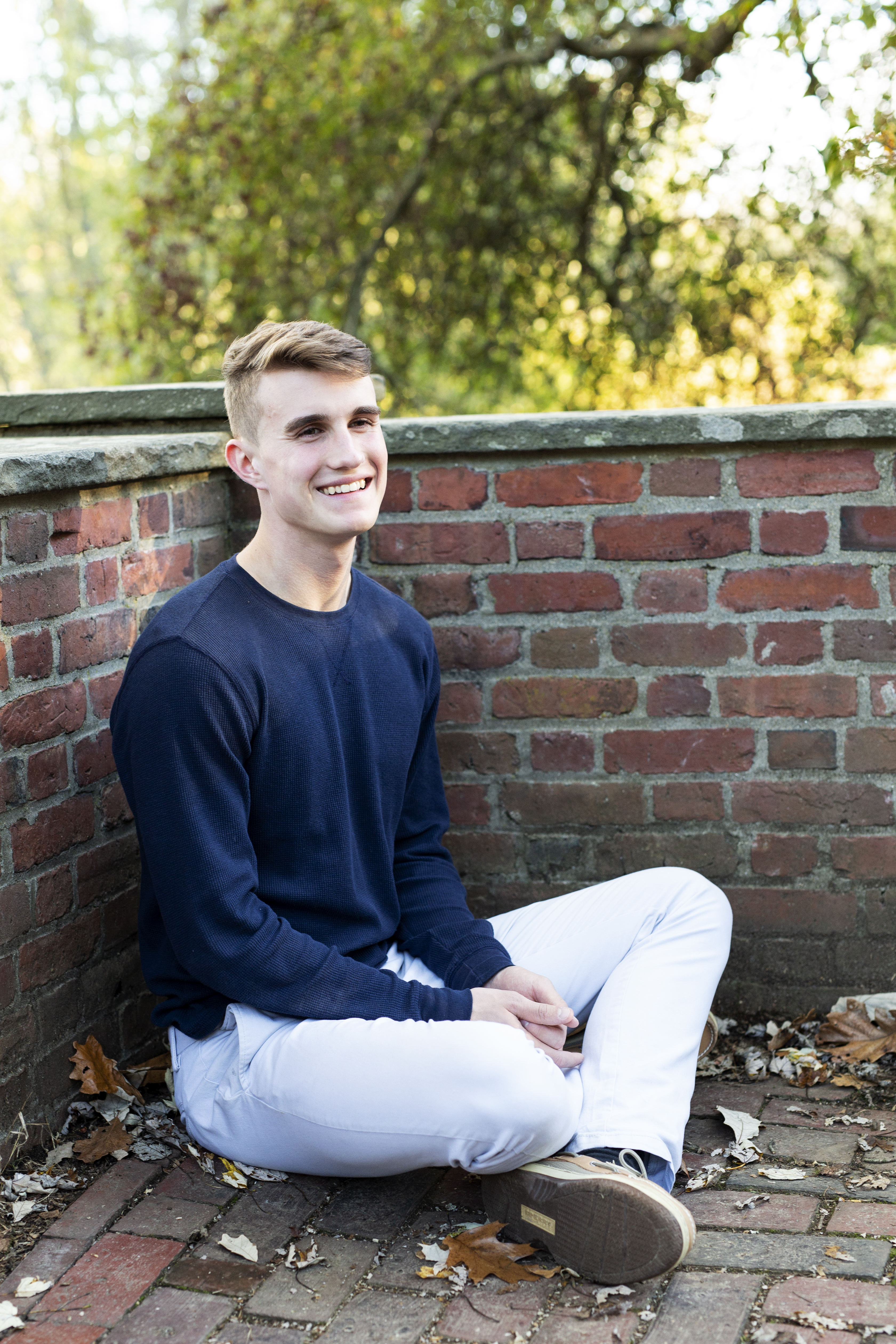 senior boy sitting by brick wall laughing