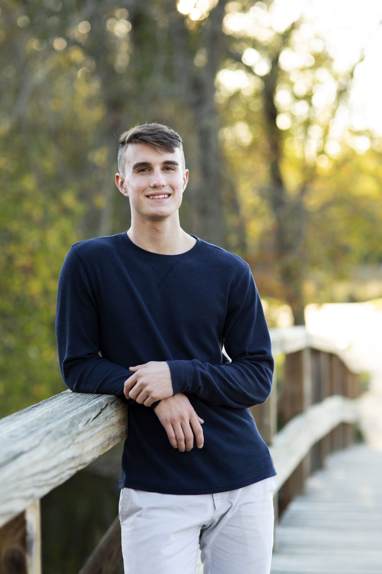 senior guy portrait leaning on wooden bridge at golden hour