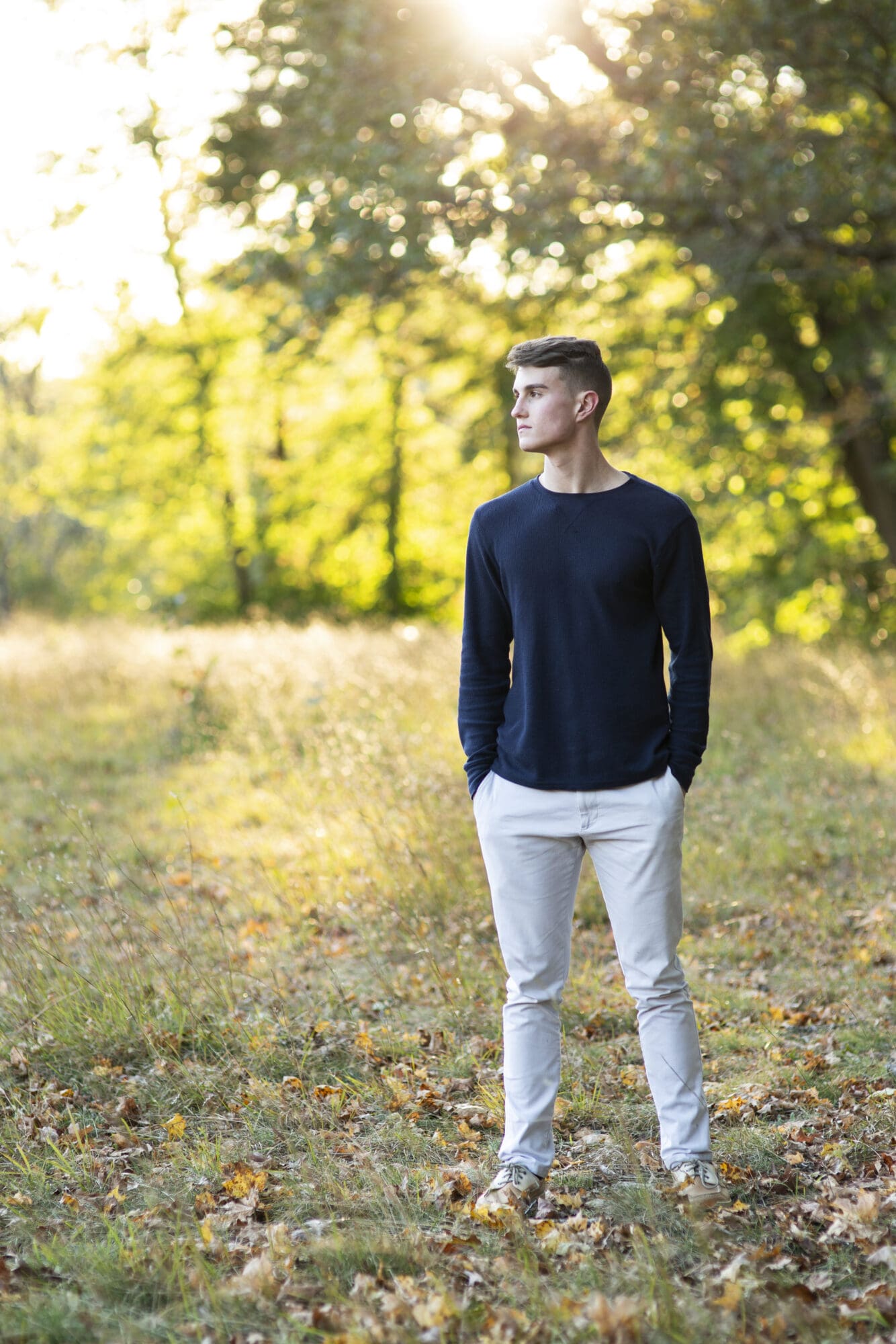 guy senior looking over shoulder standing in a field with sunlight