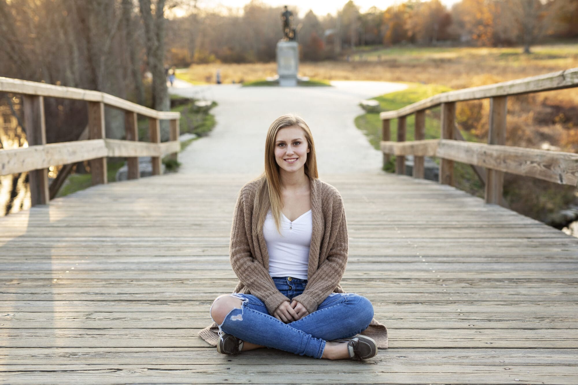 girl senior photo sitting on Old North Bridge in Concord Massachusetts at golden hour