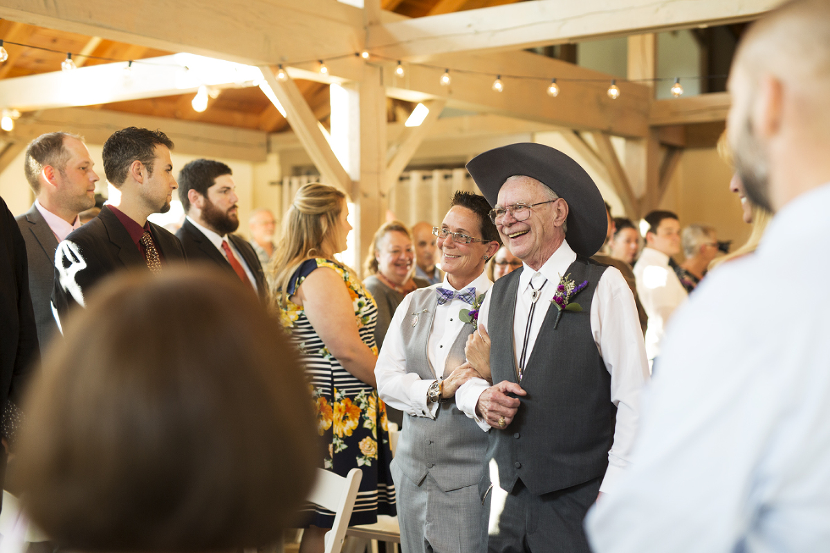 a woman walks down the aisle with her father at a lesbian same sex wedding